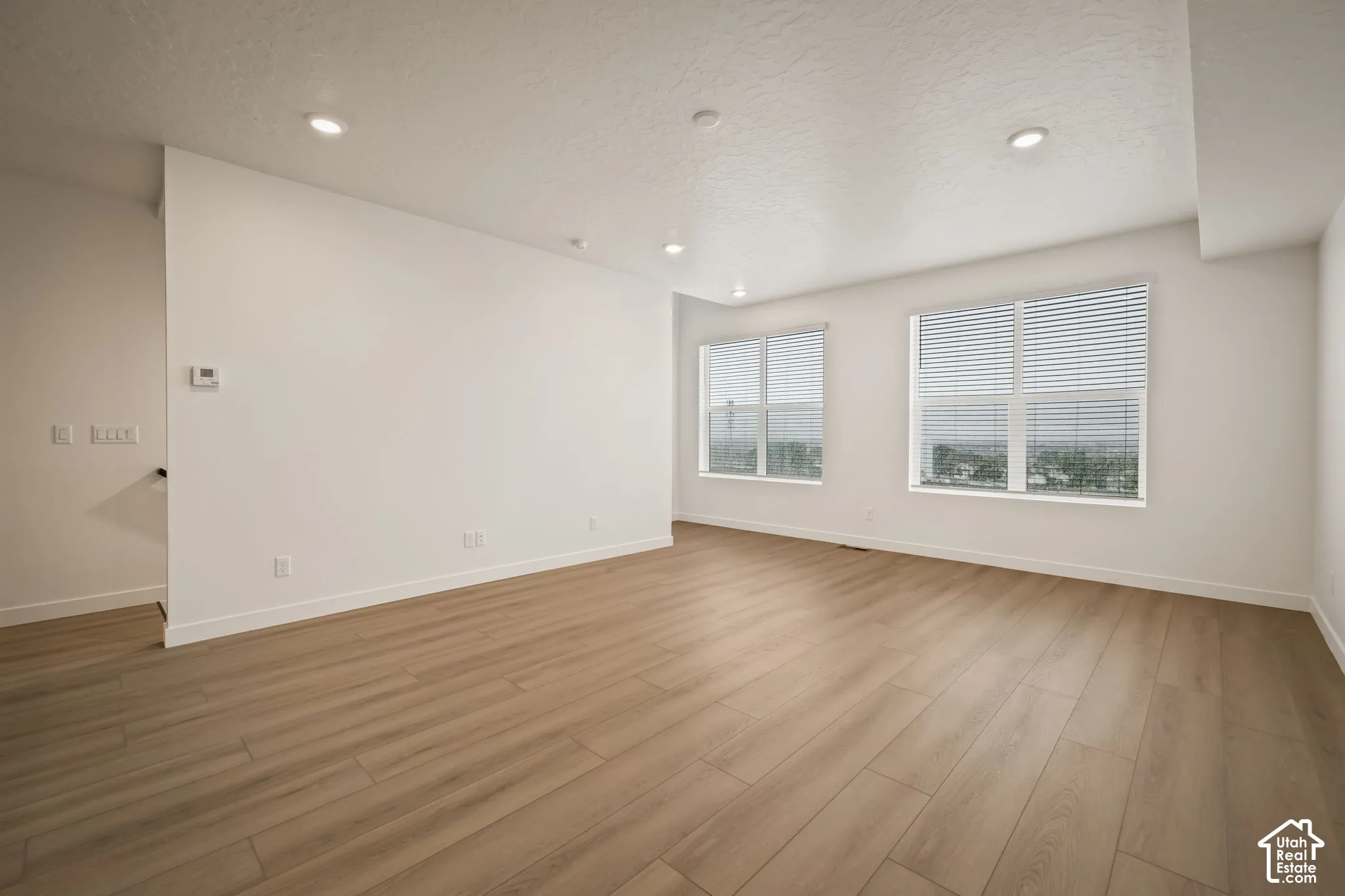 Open interior space featuring wood-finish flooring, recessed lighting, and large windows with horizontal blinds