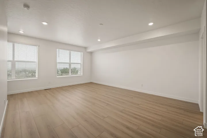 Neutral interior space featuring wood-finish flooring, recessed lighting, and large windows with integrated blinds