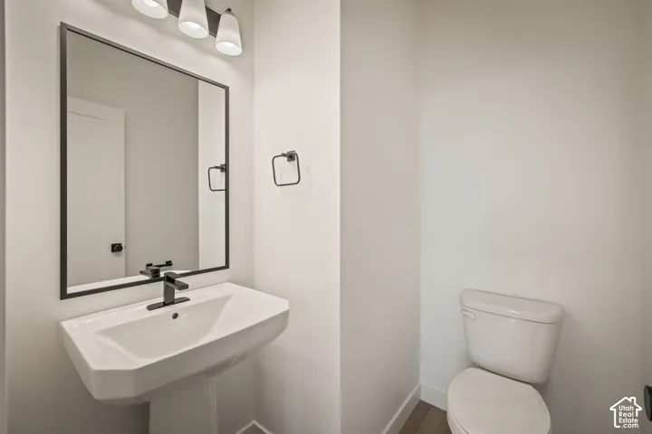 Pedestal sink with a matte black single-handle faucet, rectangular mirror with a matte black frame, three-light vanity fixture, and a standard-height toilet