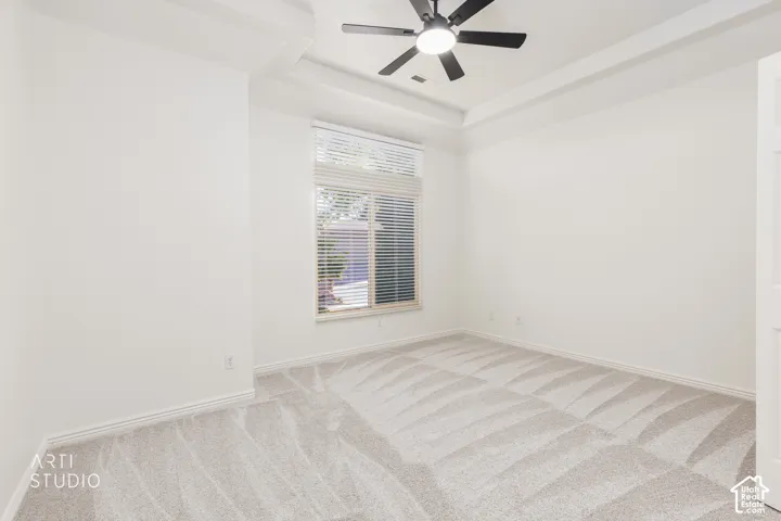 Room featuring a tray ceiling, wall-to-wall carpeting, and a multi-blade ceiling fan with integrated lighting