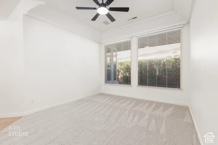 Tray ceiling featuring a central matte black ceiling fan with an integrated light fixture, carpeted flooring, and dual windows equipped with horizontal blinds