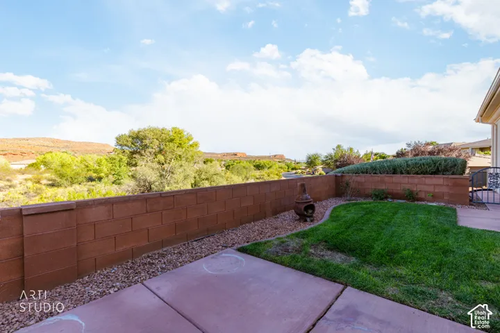 Private backyard featuring a concrete patio, a section of manicured lawn, decorative rock landscaping, and a masonry perimeter wall set against a mountain backdrop