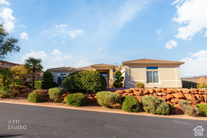 Stucco exterior featuring red rock retaining walls, manicured shrubbery, palm trees, and a tile roof