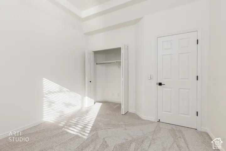 Room featuring a tray ceiling, wall-to-wall carpeting, a six-panel door with matte black hardware, and a closet with bifold doors
