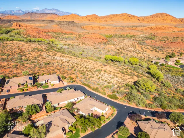 Aerial perspective of a residential neighborhood featuring asphalt streets, desert landscaping, and prominent red rock mountain scenery