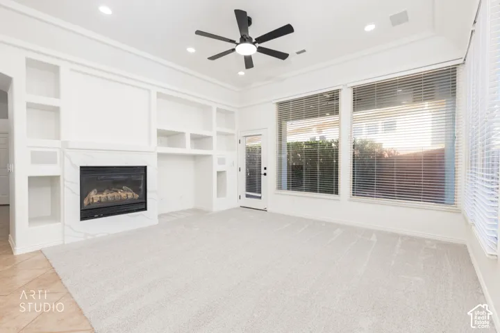 Living area featuring a floor-to-ceiling fireplace with stone-finish surround, custom built-in shelving, tray ceiling, recessed lighting, and wall-to-wall windows