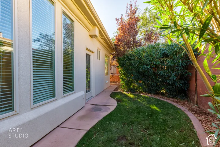 Stucco exterior featuring full-height windows, a glass-panel door, concrete patio, and landscaped perimeter