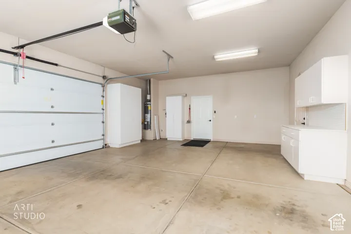 Two-car garage featuring a concrete floor, built-in white cabinetry, automated door opener, and fluorescent lighting