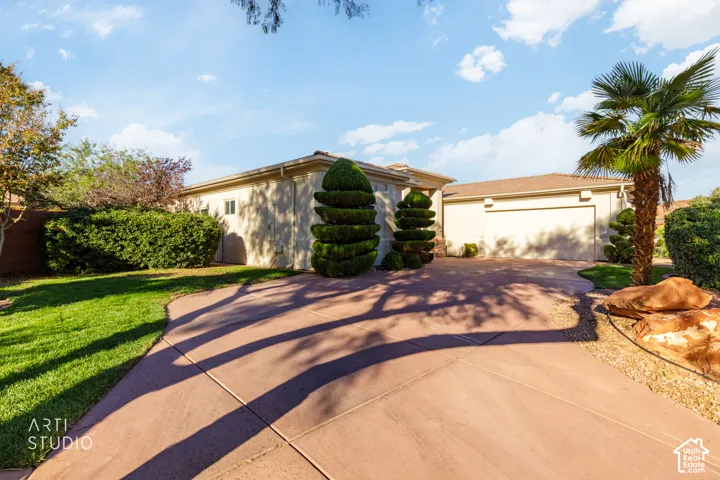 Stucco exterior with an attached multi-car garage, concrete driveway, and landscaped lawn featuring mature shrubbery and palm trees