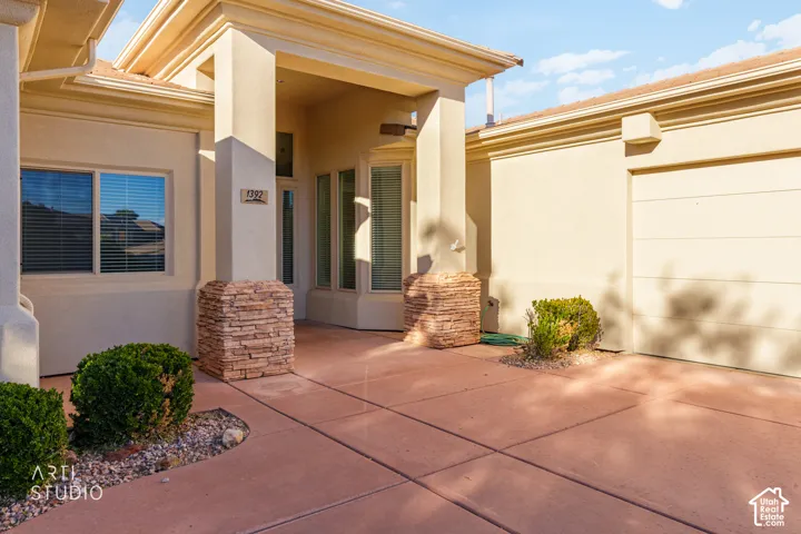 Stucco exterior featuring stacked stone column bases, a covered recessed entryway, and a multi-pane bay window