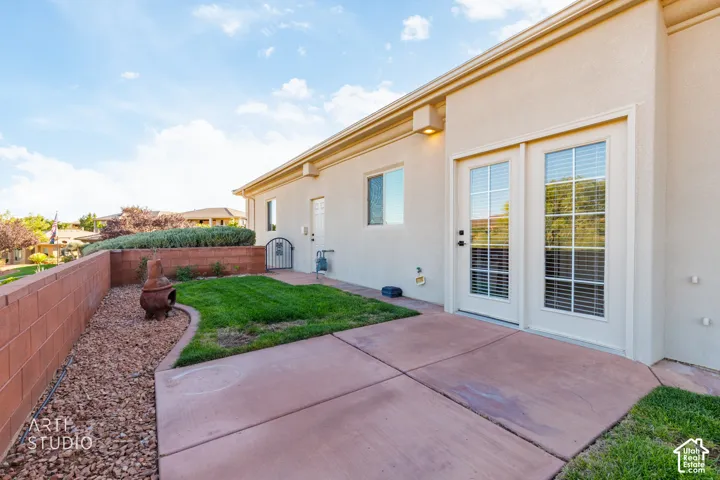 Stucco exterior featuring a concrete patio, landscaped grass area, decorative stone perimeter wall, and double glass-panel doors