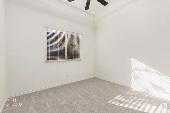 Room featuring neutral wall-to-wall carpeting, tray ceiling, and a ceiling fan