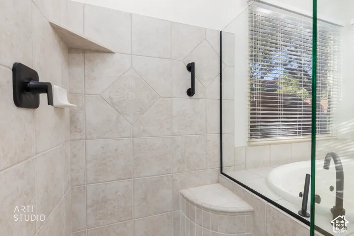 Shower featuring neutral-toned tile work with decorative inset detailing, a built-in corner bench, matte black hardware, and a glass-enclosed soaking tub