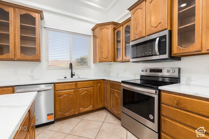 Kitchen featuring natural wood-finish cabinetry, stainless steel appliances, stone-patterned countertops, a matte black faucet, and ceramic tile flooring