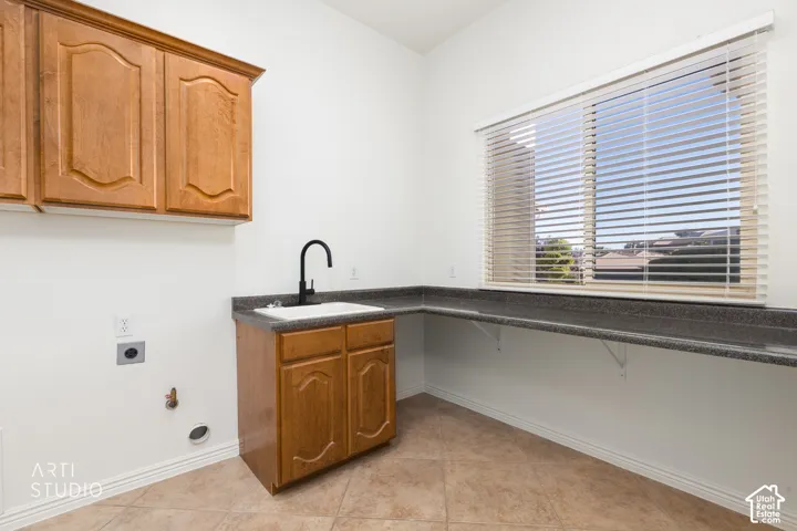 Utility area featuring wood-finish cabinetry, a drop-in sink with a matte black faucet, extended stone-finish countertop, and tile flooring