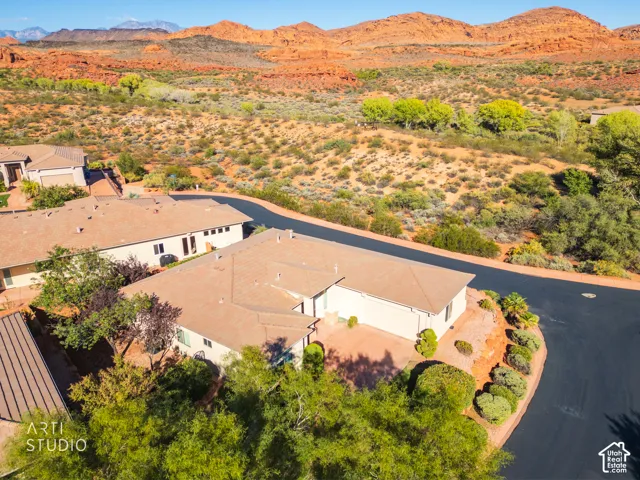 Single-story residence featuring a tile roof, light-toned exterior finish, attached multi-car garage, and desert landscaping, situated against a backdrop of red rock formations