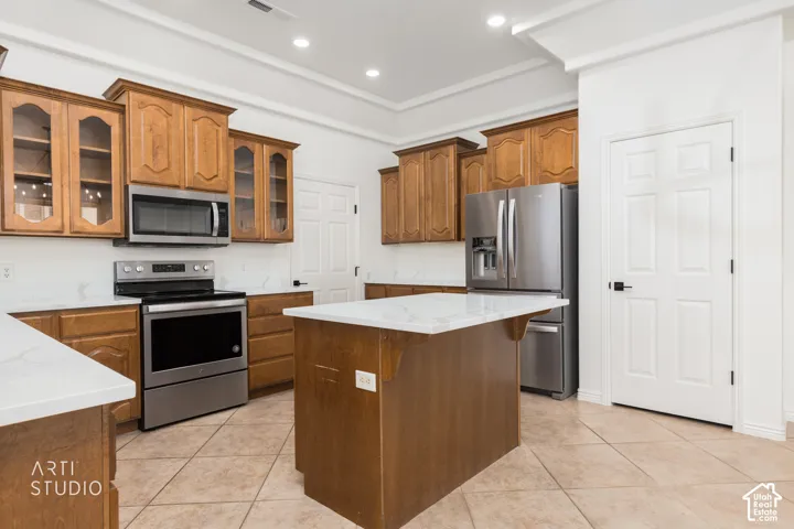 Kitchen featuring stained wood cabinetry, stone-finish countertops, stainless steel appliances, a central island, and ceramic tile flooring