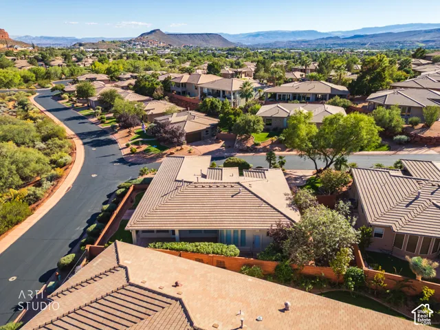 Aerial perspective featuring a tile-roof residence with a covered patio, set against a backdrop of desert mountains and mature landscaping