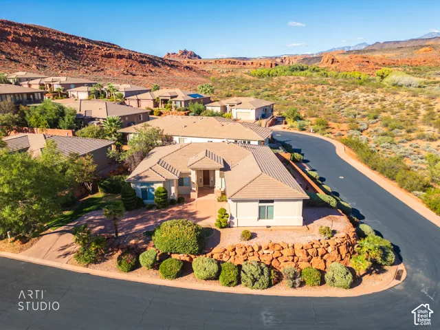 Single-story residence featuring a tile roof, neutral stucco exterior, circular paver driveway, and natural rock retaining walls set against a desert mountain backdrop