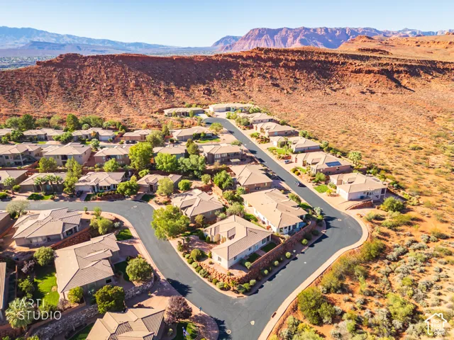 Aerial perspective of a residential community featuring red rock desert topography, paved streets, and expansive mountain terrain