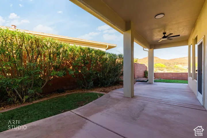 Covered concrete patio featuring a ceiling fan, recessed lighting, and a landscaped yard with mature shrubbery and masonry perimeter walls
