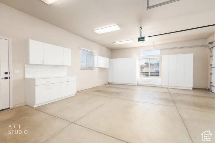 Garage space featuring extensive white built-in cabinetry, smooth concrete flooring, overhead fluorescent lighting, and integrated pegboard wall storage