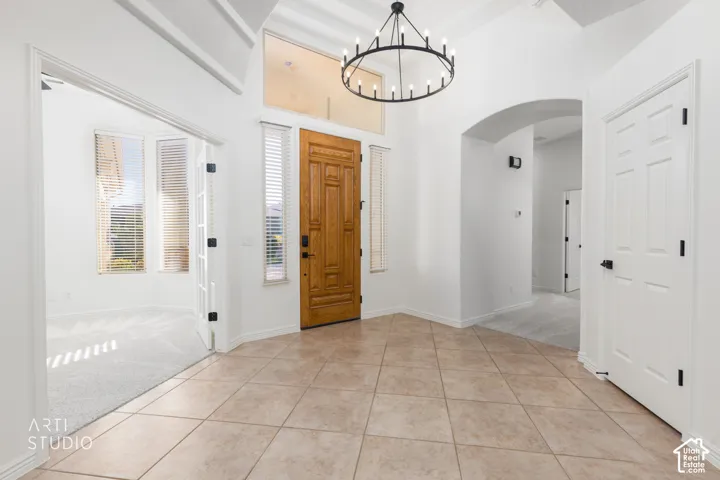 Foyer featuring ceramic tile flooring, a natural wood entry door, a transom window, sidelights, and a tiered metal chandelier