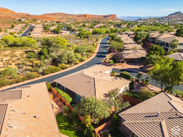 Aerial perspective featuring a tile roof, paved driveway, enclosed lawn area, and desert landscape set against a mountain backdrop