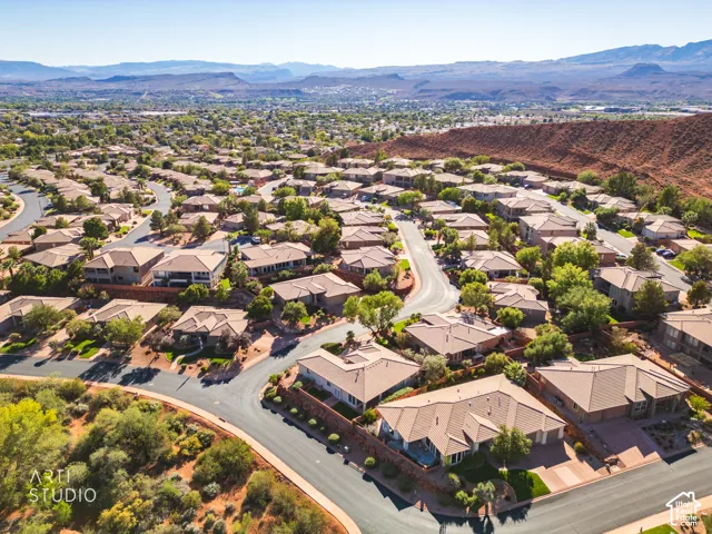 Aerial perspective of a residential neighborhood featuring paved asphalt roadways, xeriscaped lots, and prominent red rock mountain backdrops