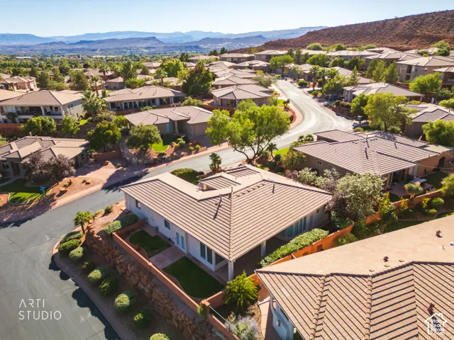 Aerial perspective featuring a tile roof, built-in covered patio, tiered stone retaining wall, and landscaped grass area against a backdrop of desert mountains