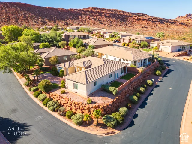 Corner lot residence featuring a tile roof, stucco exterior, tiered rock retaining walls, and desert landscape elements set against a mountain backdrop