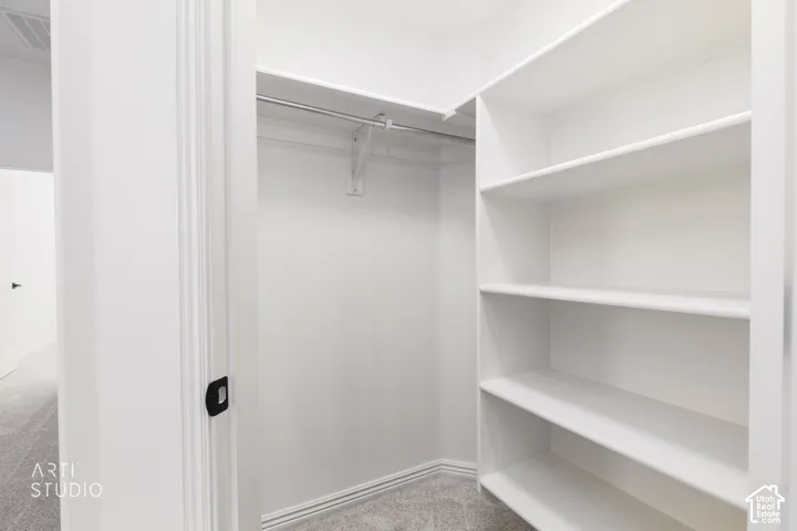 Walk-in closet featuring white built-in shelving and a metal garment rod