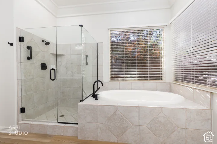 Glass-enclosed shower with matte black fixtures, integrated tile-surround soaking tub, neutral ceramic tile detailing, and wood-finish flooring
