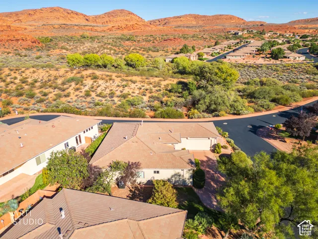 Aerial perspective featuring a single-story residence with a multi-gabled roof, paved driveway, and expansive sandstone mountain backdrop