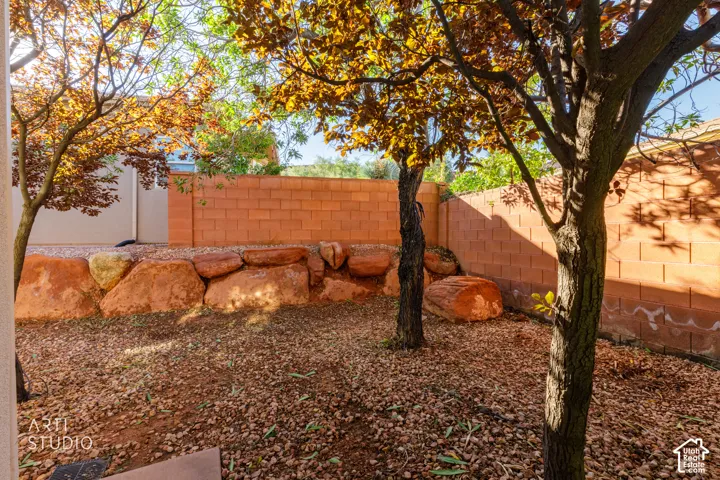 Outdoor space featuring a masonry perimeter wall, natural stone boulder retaining wall, and mature trees