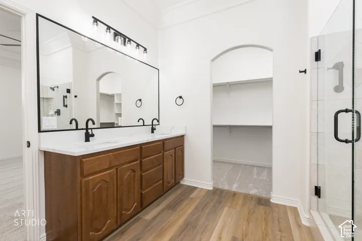 Primary bathroom featuring a wood-finish vanity with dual sinks and matte black fixtures, large framed mirror, ceramic tile surround, walk-in shower with glass enclosure and black hardware, and built-in shelving niche