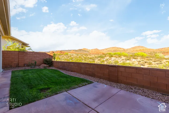 Rear patio featuring a paved surface, a grass lawn, decorative gravel, and a masonry perimeter wall with a mountain backdrop