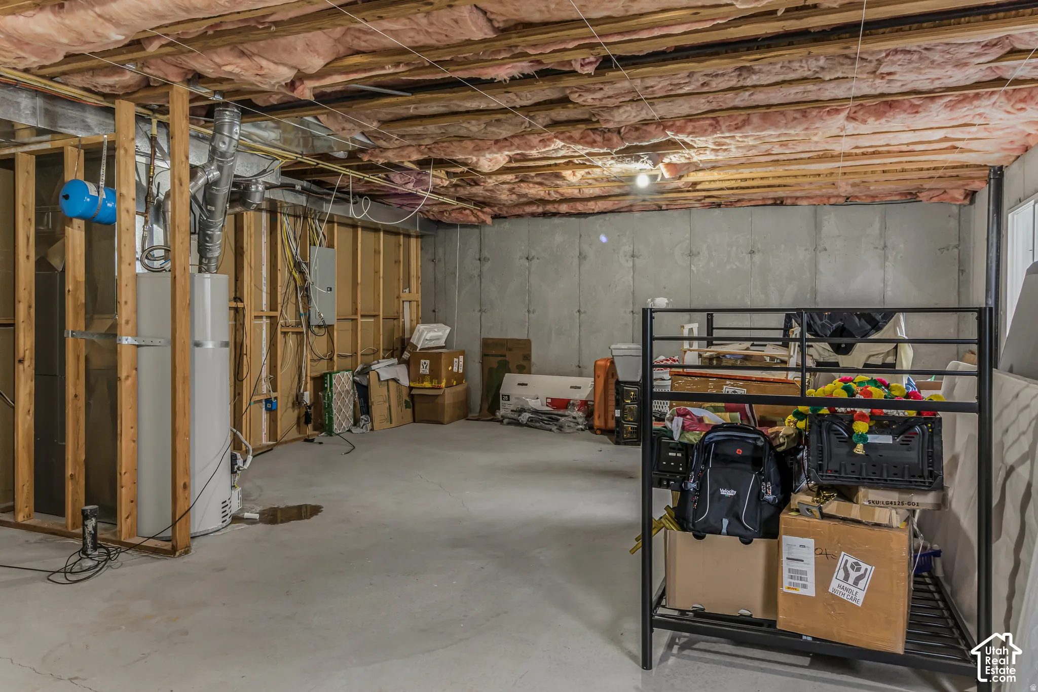 Unfinished basement featuring exposed wood framing, concrete foundation walls, concrete floor, and fiberglass insulation