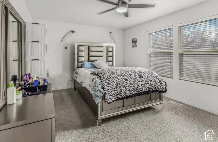Neutral-toned carpeted flooring, dual windows with horizontal blinds, and a central ceiling fan with integrated lighting