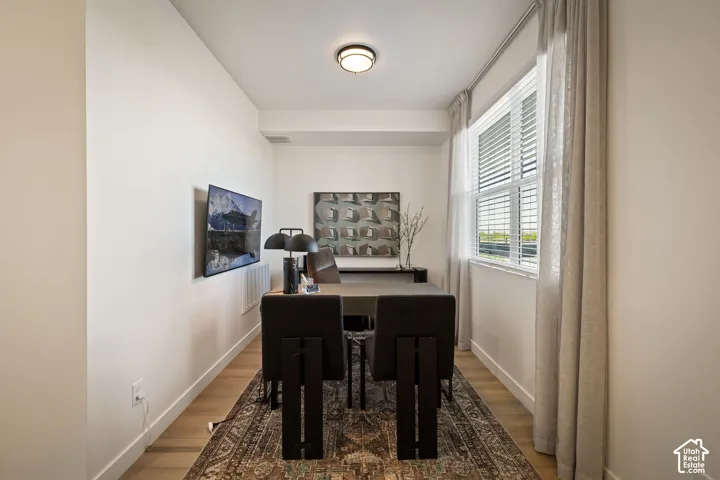 Interior space featuring wood-finish flooring, a large window with horizontal blinds, and a circular flush-mount ceiling light fixture
