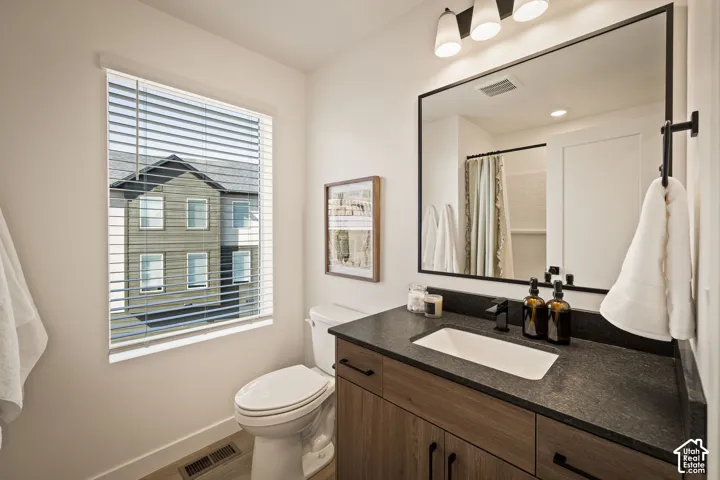Vanity featuring a dark stone-finish countertop, rectangular undermount sink, and wood-finish cabinetry with matte black hardware