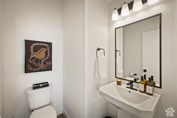 Powder room featuring a wall-mounted mirror with a black metal frame, a pedestal sink with a matte black faucet, and a four-light fixture with frosted glass shades