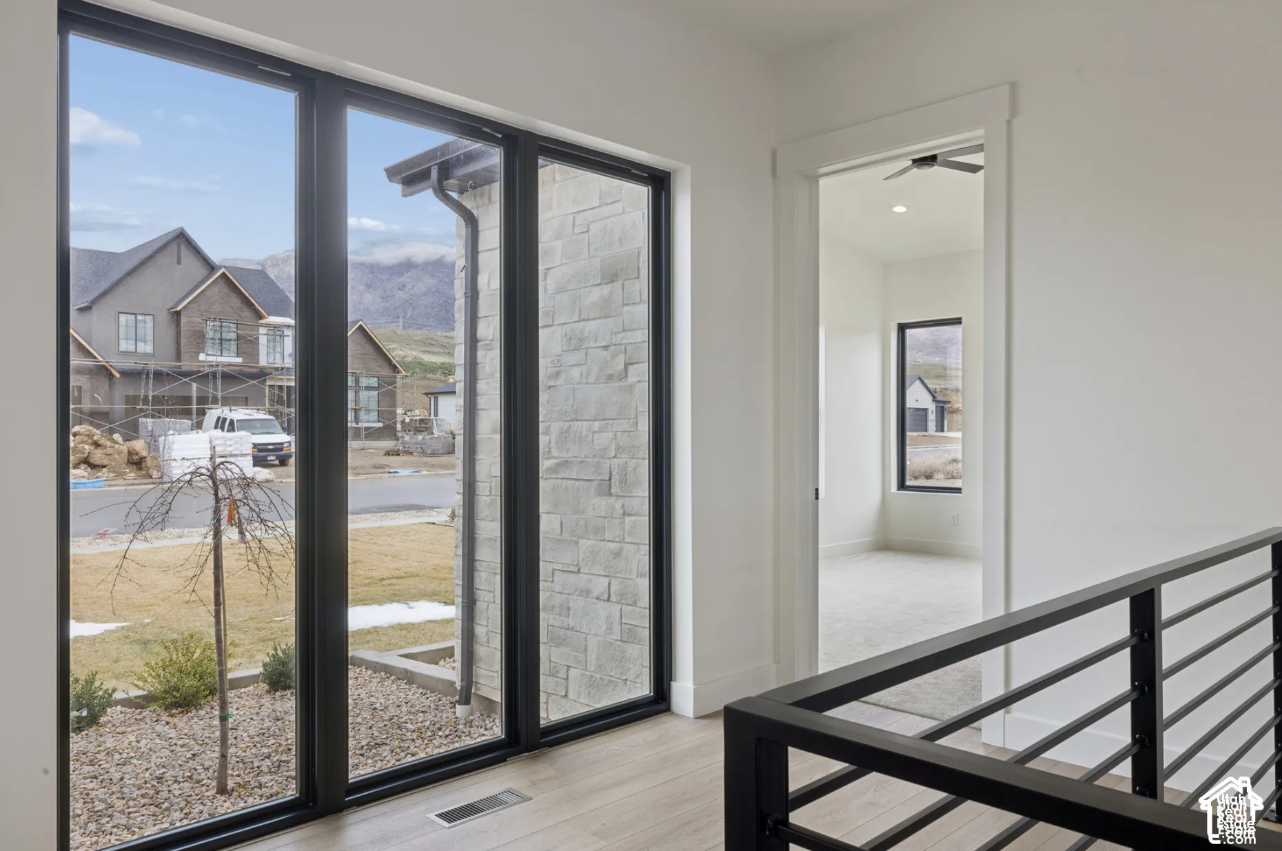 Floor-to-ceiling black-framed windows, metal horizontal railing, and light-tone wood-finish flooring