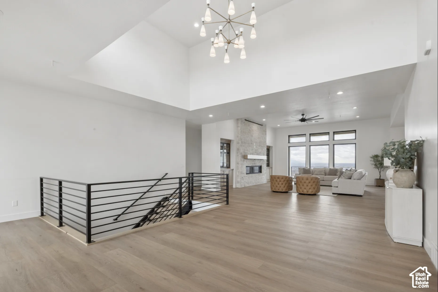 Vaulted ceiling with contemporary chandelier, wood-finish flooring, floor-to-ceiling stone-surround fireplace, and metal-railing staircase