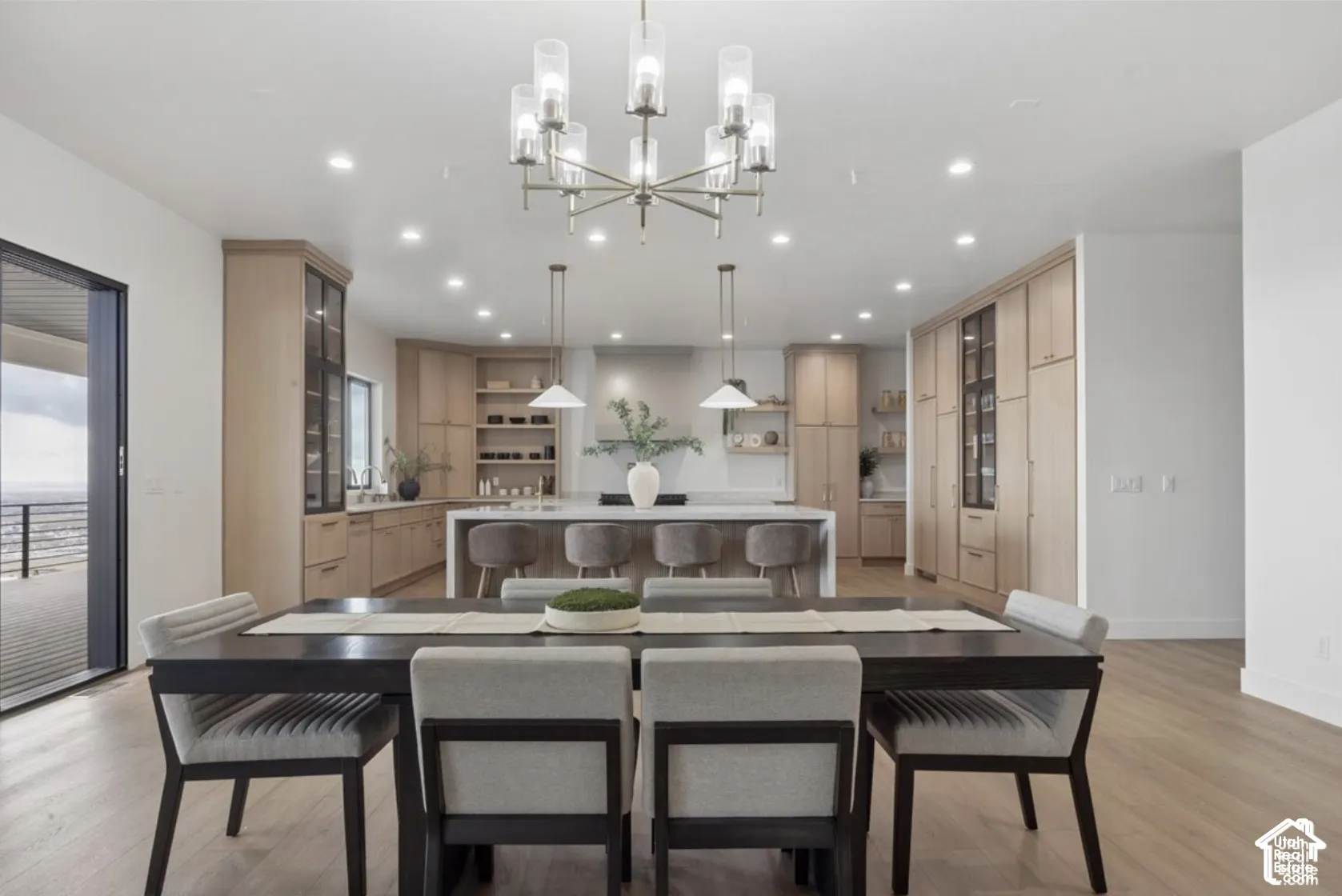 Modern kitchen featuring wood-finish cabinetry, a large central island with integrated seating, recessed lighting, and a multi-arm chandelier