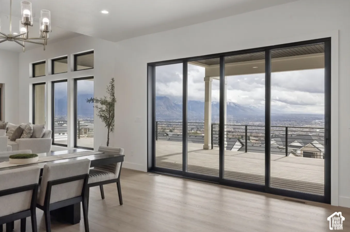 Large sliding glass doors with black frames, wood-finish flooring, multi-pane floor-to-ceiling windows, and a multi-arm chandelier