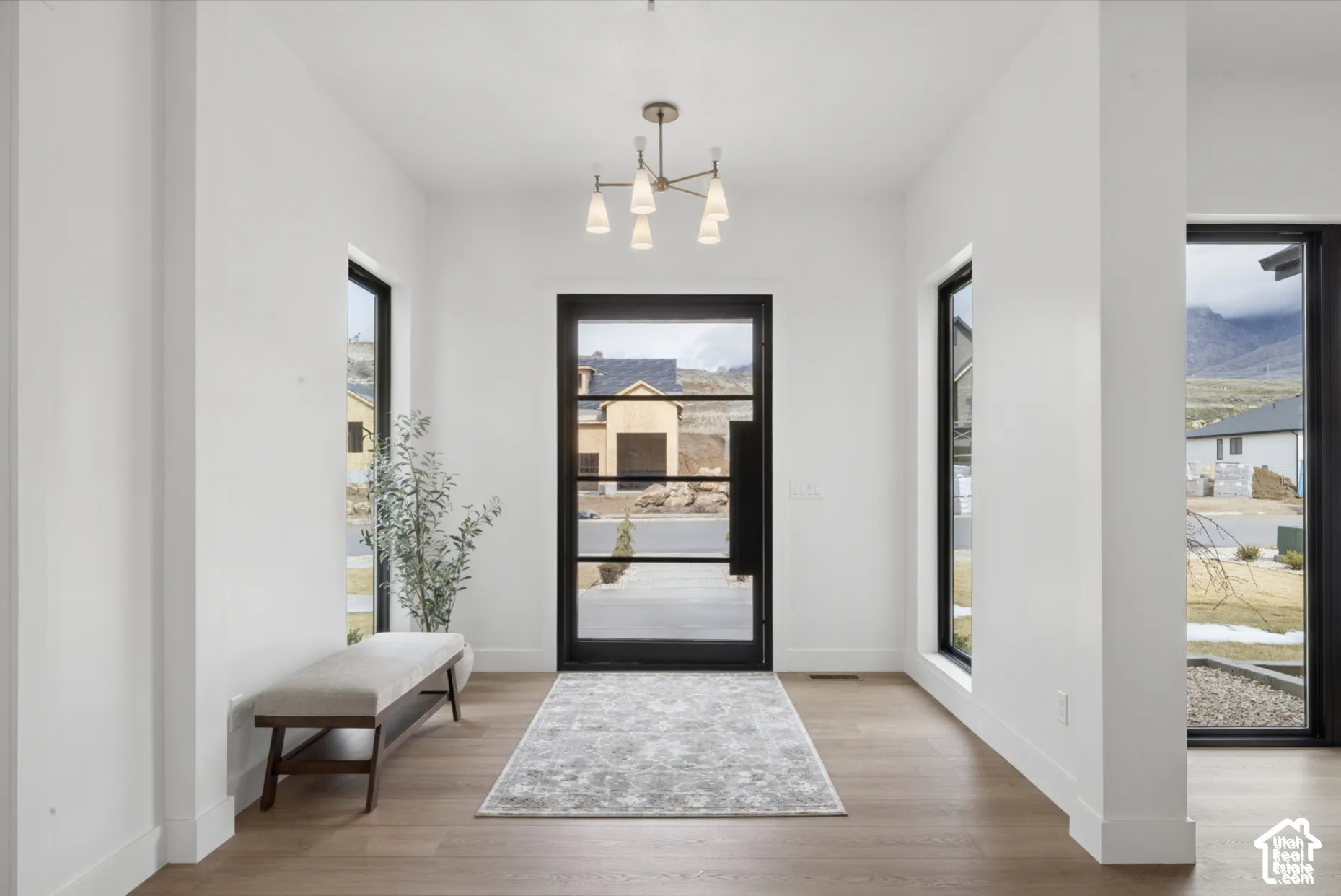 Foyer featuring wood-finish flooring, a contemporary six-arm chandelier, and a black-framed glass entry door flanked by tall vertical windows