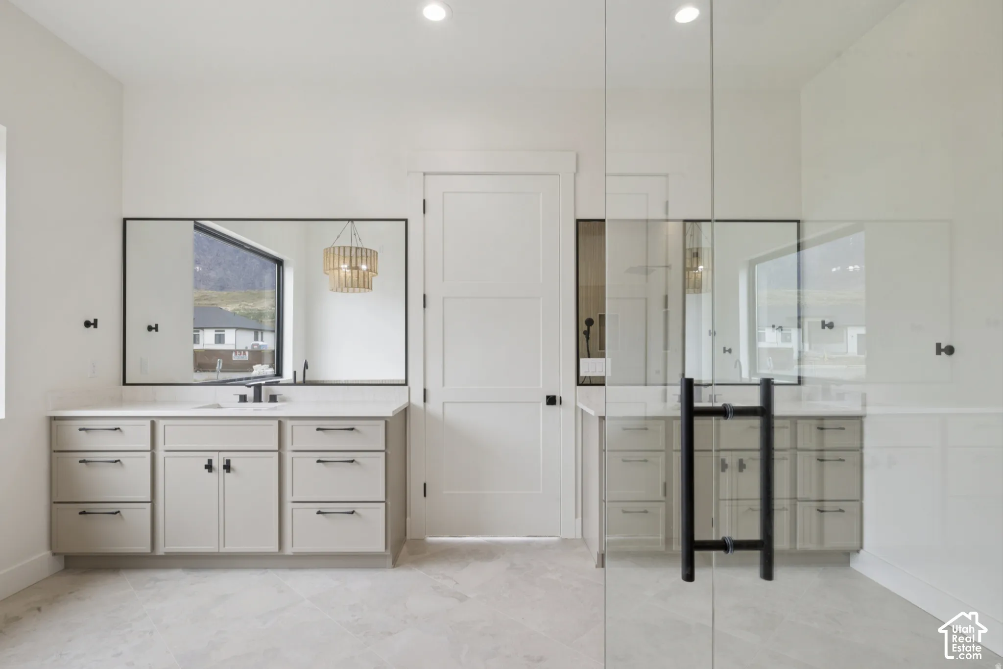 Dual vanities featuring soft-close cabinetry, light-toned stone countertops, framed mirrors, and black hardware, complemented by a glass-enclosed shower with matte black fixtures