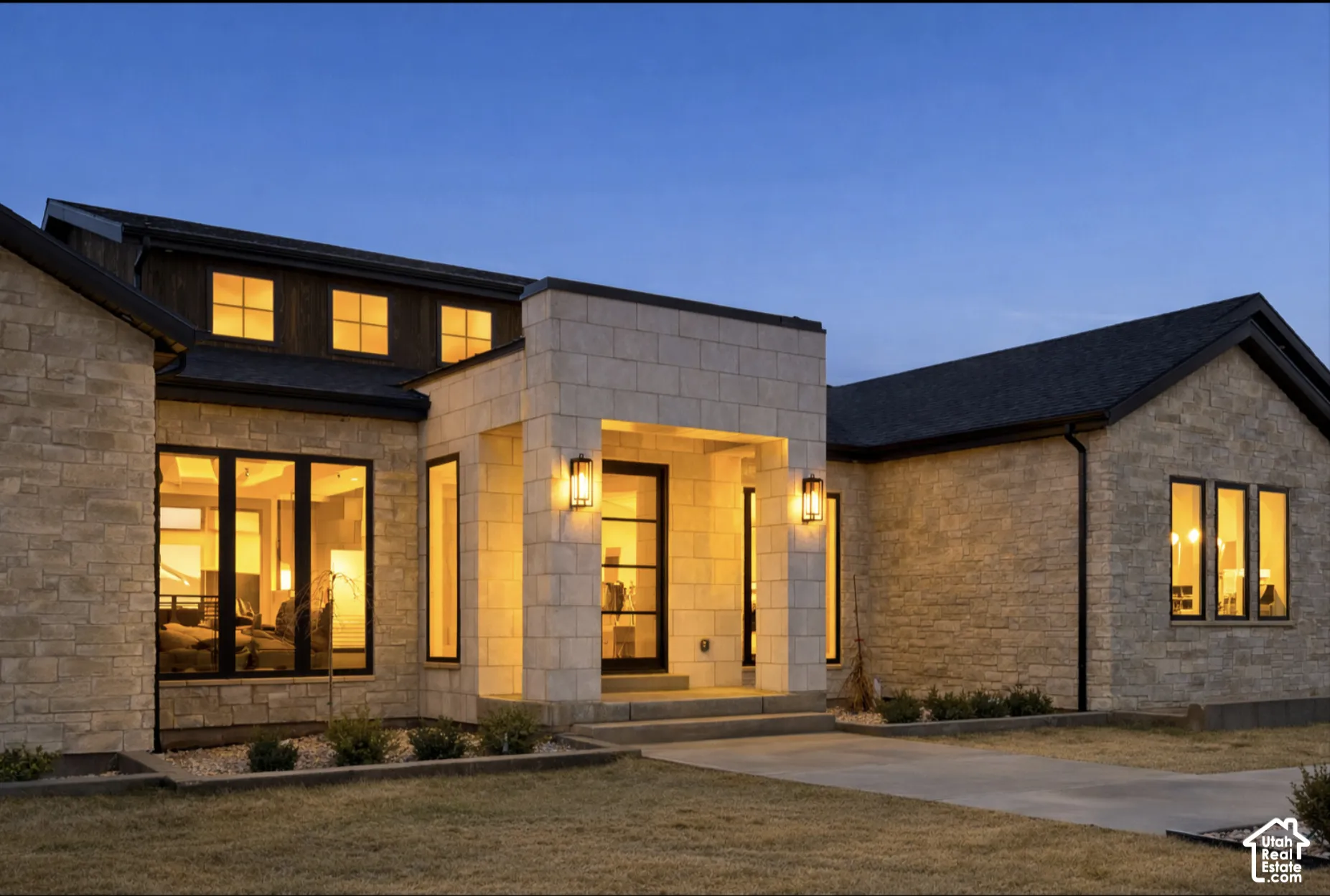 Contemporary exterior featuring stacked stone masonry, a recessed entryway with block pillar details, dark-trimmed grid windows, and multi-pitched rooflines