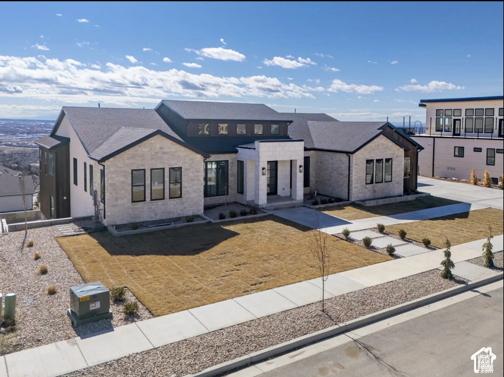Contemporary exterior featuring light-colored stone masonry, dark-toned vertical siding, a multi-gabled asphalt shingle roof, transom windows, and a concrete paver walkway